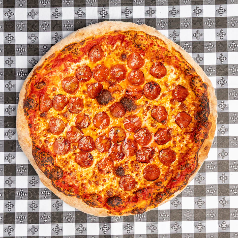 Overhead view of a pepperoni pizza with melted cheese and charred crust on a black-and-white patterned tablecloth.
