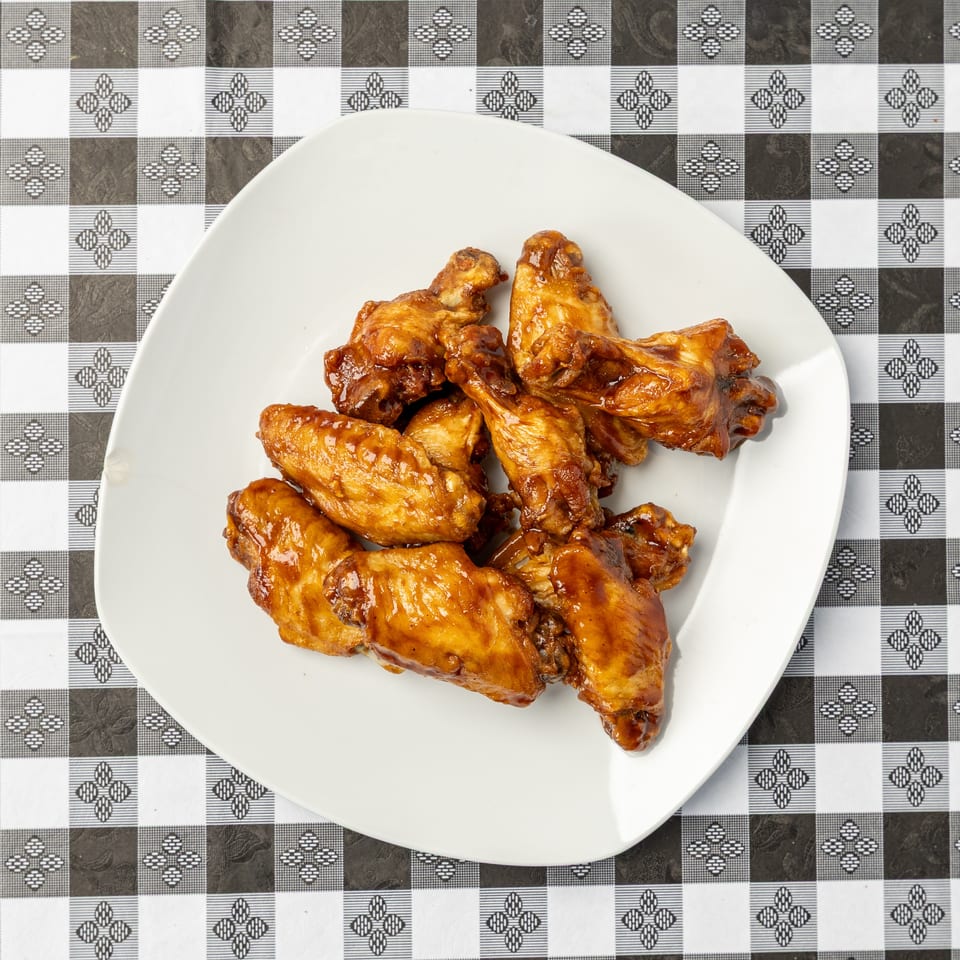 Plate of glossy roasted chicken wings on a black-and-white patterned tablecloth.