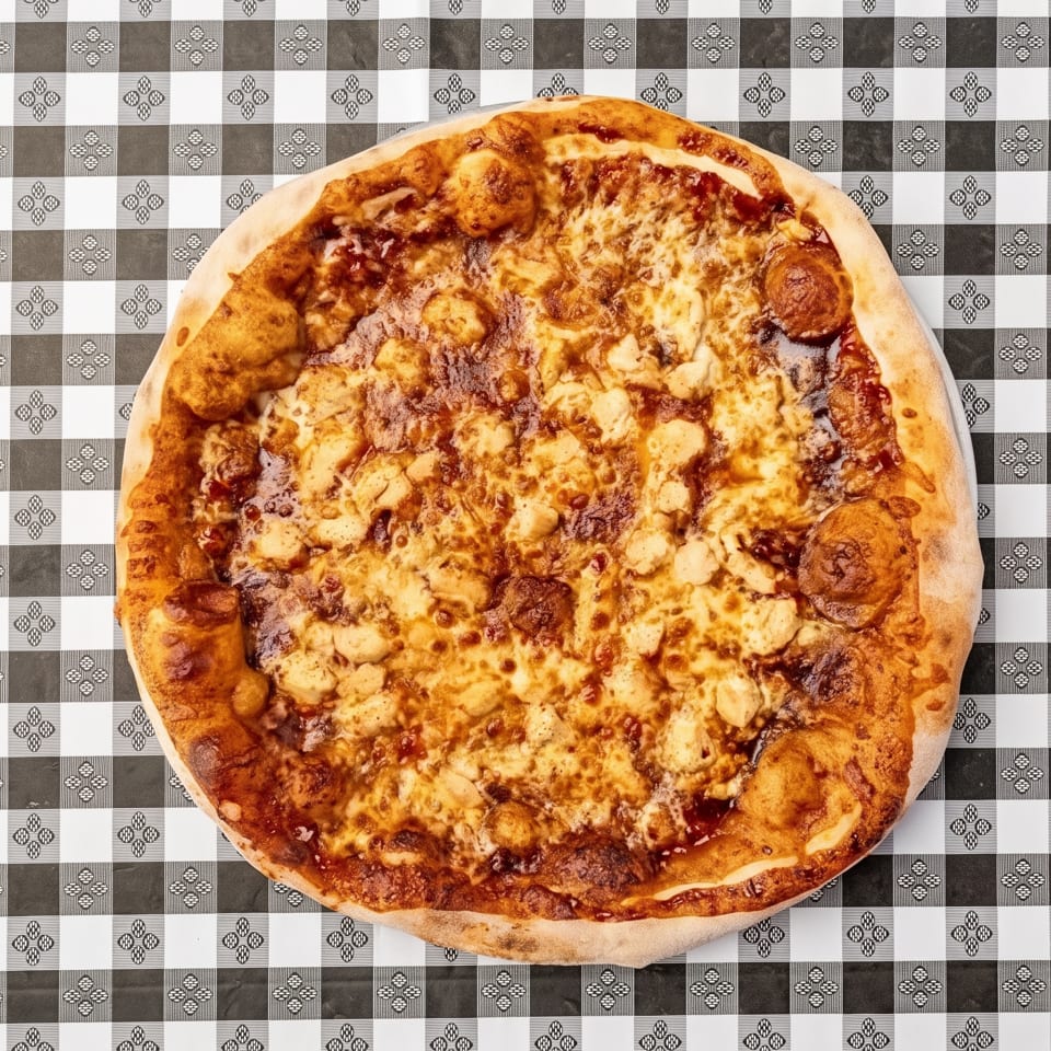 Large cheese-and-pepperoni pizza with a thick crust on a black-and-white patterned tablecloth.