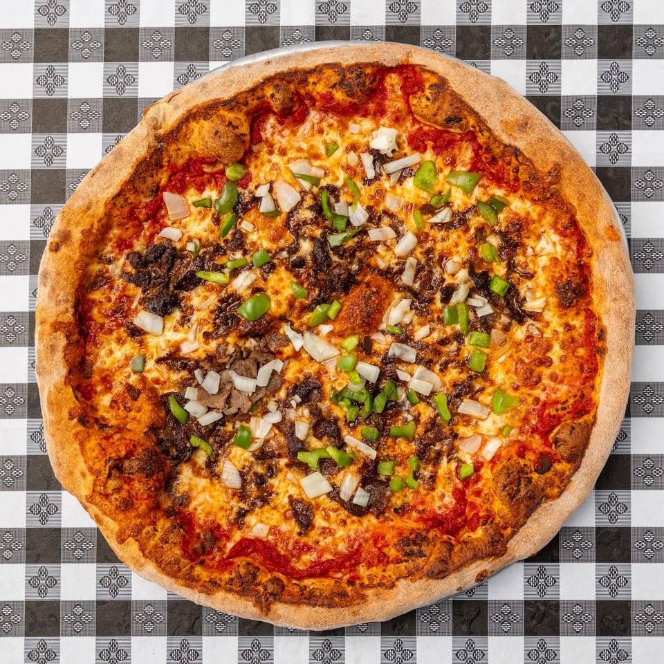 Large cheese pizza topped with ground meat, green peppers, and onions on a black-and-white checkered tablecloth.