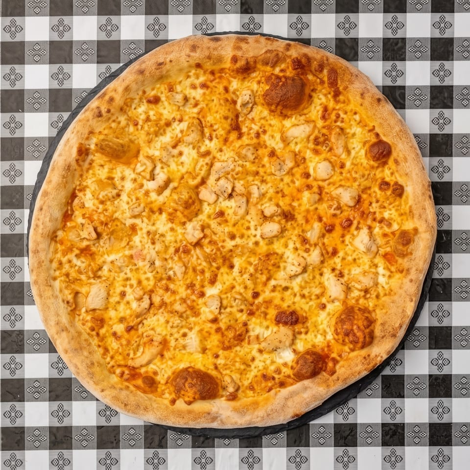 Cheesy pizza topped with pepperoni and diced chicken on a black-and-white patterned tablecloth.